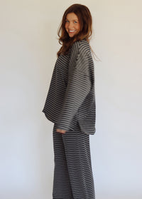 A woman modeling a matching two-piece loungewear set consisting of a long-sleeve top and wide-leg pants, both featuring a navy and white horizontal stripe pattern, set against a plain white studio background.