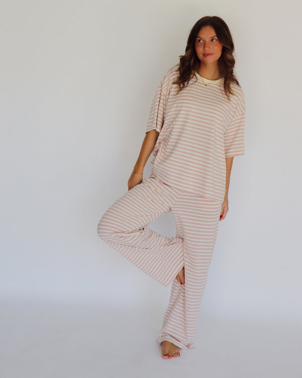 A woman modeling a matching two-piece loungewear set with short-sleeve top and wide-leg pants, featuring horizontal stripes in a light pink and off-white color, set against a plain white studio background.