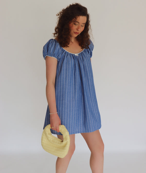 Woman wearing a blue striped dress holding a yellow bag against a plain background